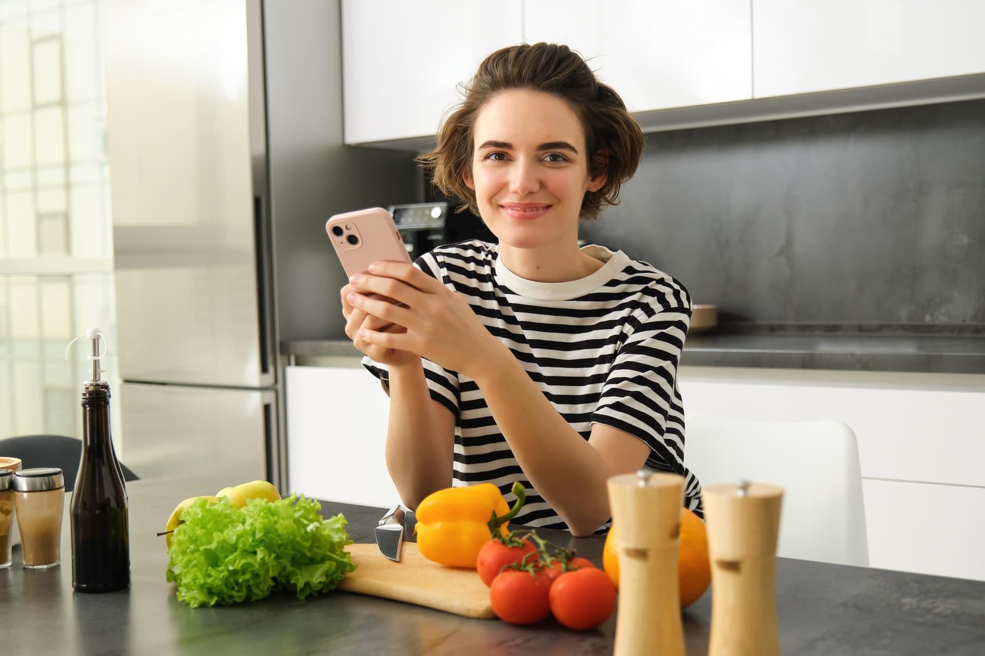 Mulher usando celular para registrar refeição saudável na cozinha